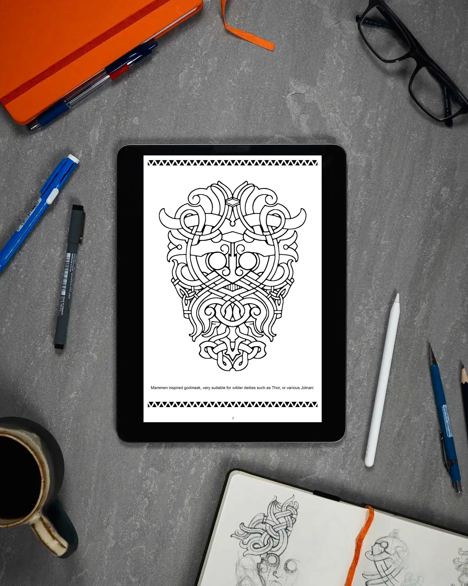 Mammen inspired Viking godmask tattoo design on tablet, ideal for Thor or Jotnar, surrounded by sketch tools and notebook.