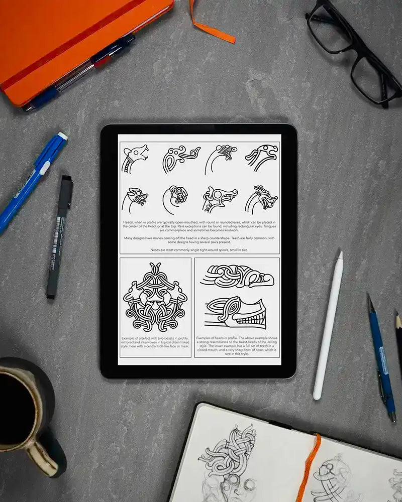 Viking tattoo design guide on tablet with Norse knotwork sketches, pens, and coffee — ideal for tattoo artists and enthusiasts.