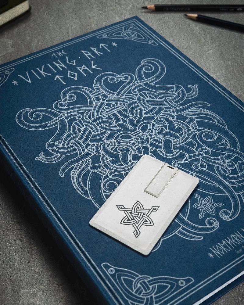 The Viking Art Tome book with Norse knotwork design and rune-inscribed stone token on dark surface