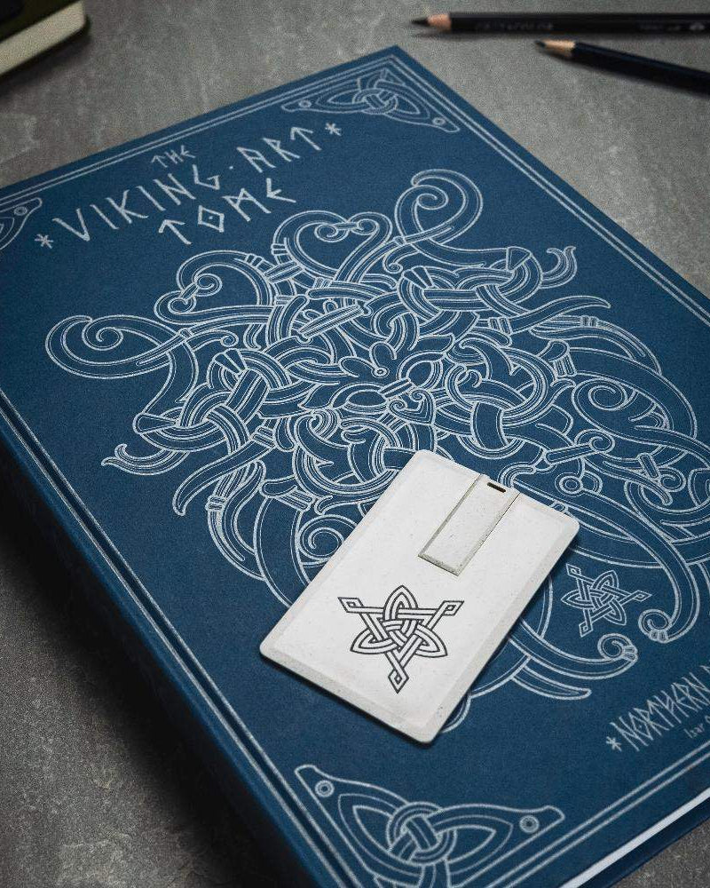 The Viking Art Tome book with Norse knotwork design and rune-inscribed stone token on dark surface