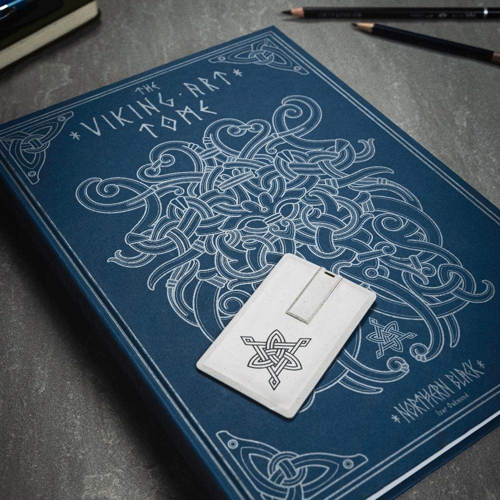 The Viking Art Tome book with Norse knotwork design and rune-inscribed stone token on dark surface
