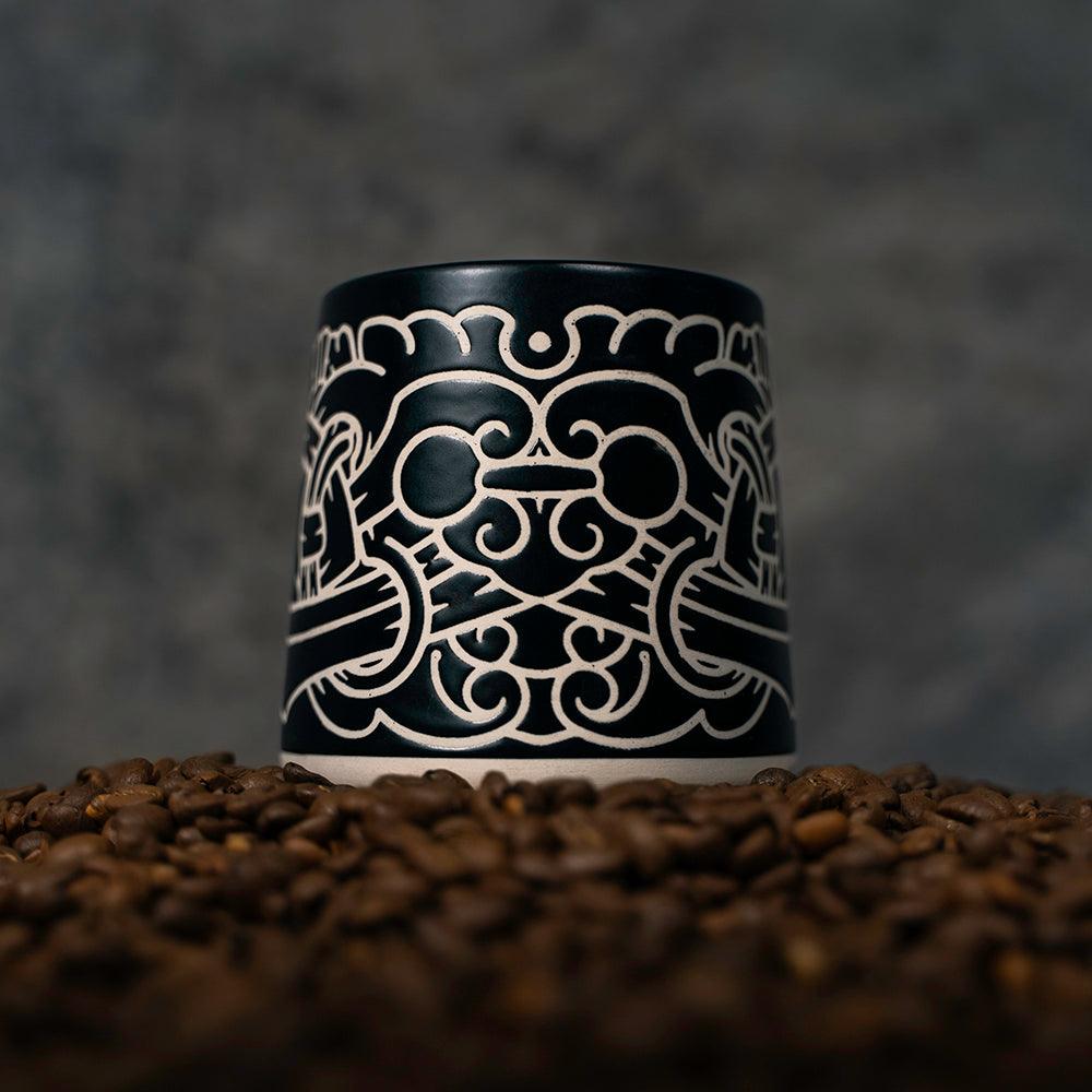 Black ceramic mug with intricate Norse-inspired Viking art design, set on coffee beans
