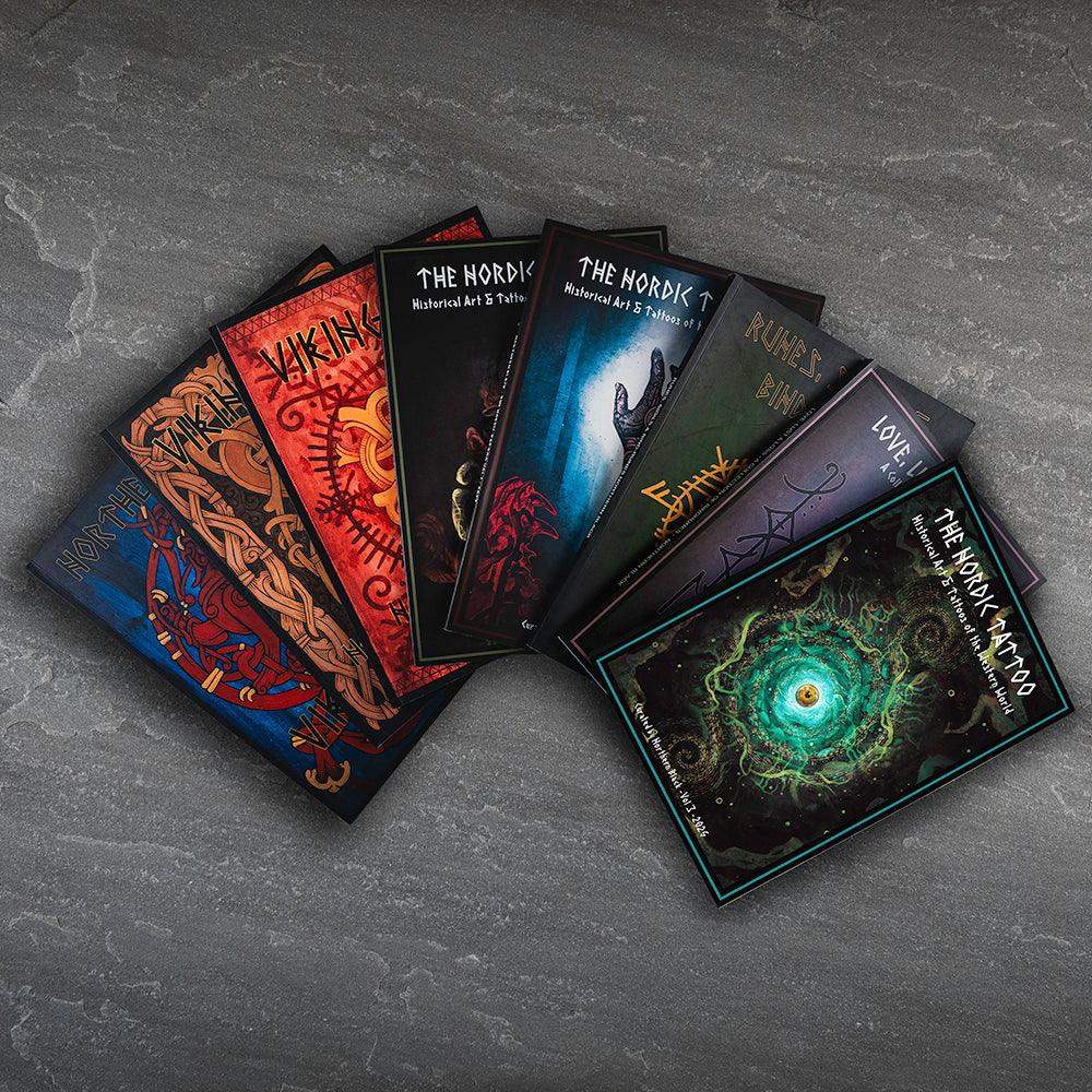 Viking tattoo art books with Norse designs, runes, and historical motifs fanned on stone surface