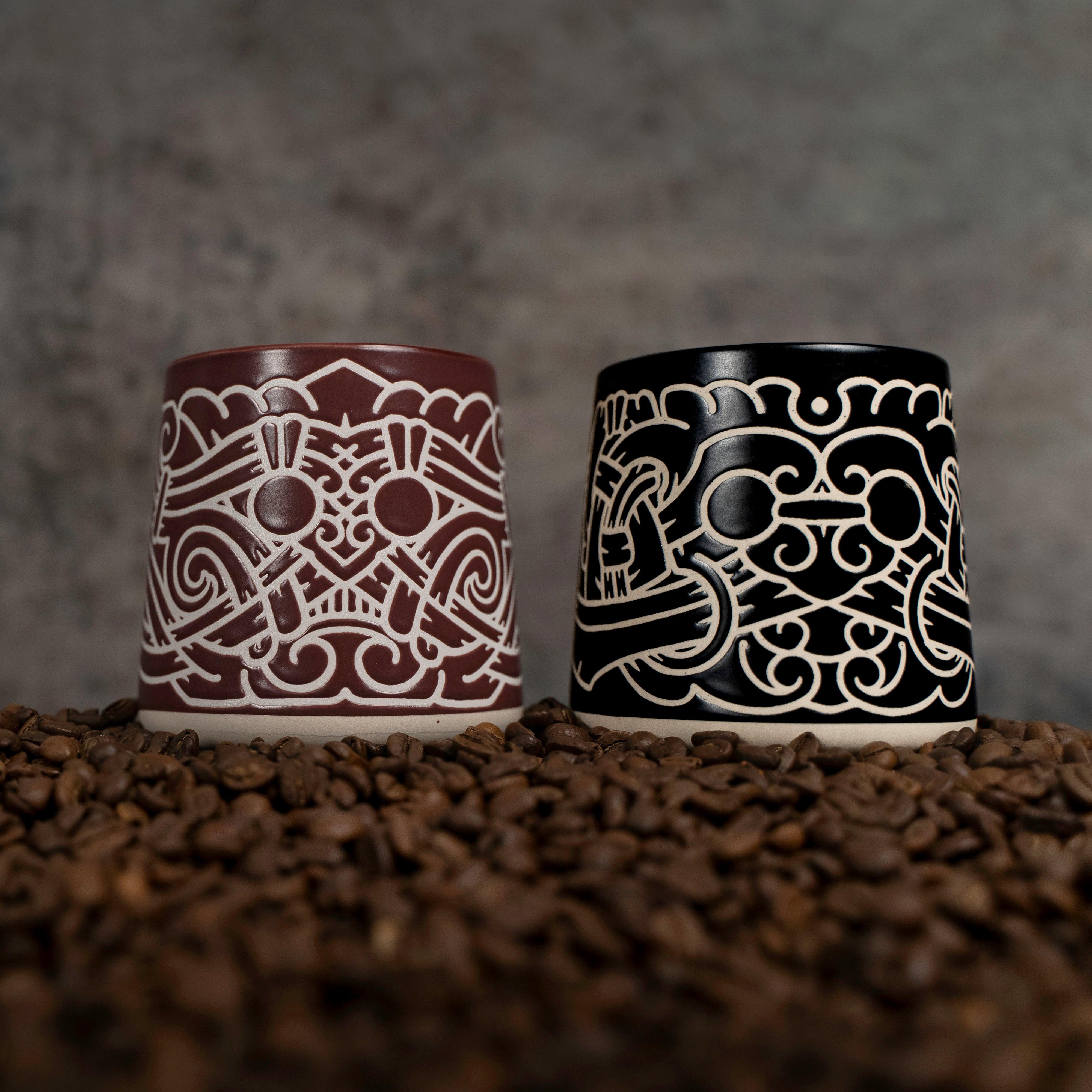 Two Viking-inspired ceramic mugs with Norse knotwork designs, set on coffee beans.