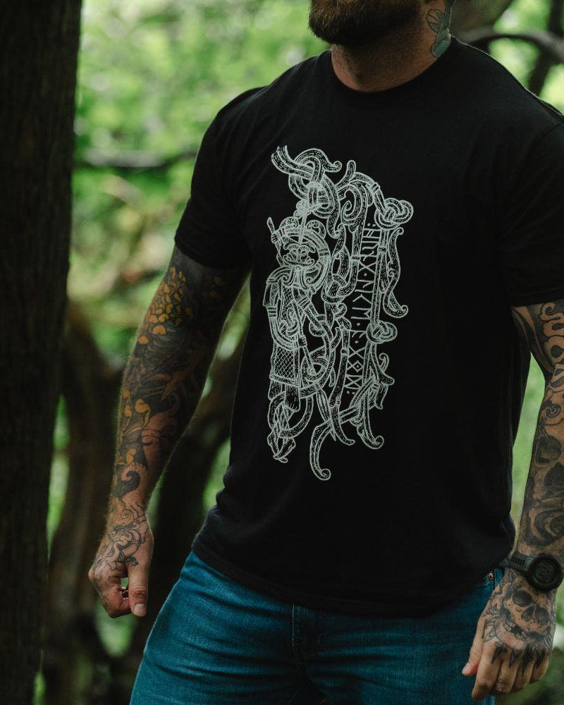 Man in forest wearing black t-shirt with intricate Norse Viking tattoo-inspired design and runes