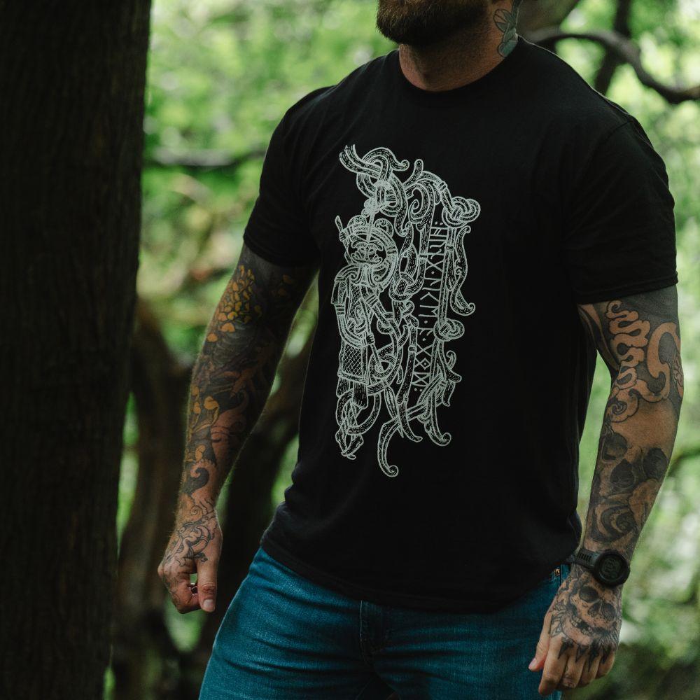 Man in forest wearing black t-shirt with intricate Norse Viking tattoo-inspired design and runes