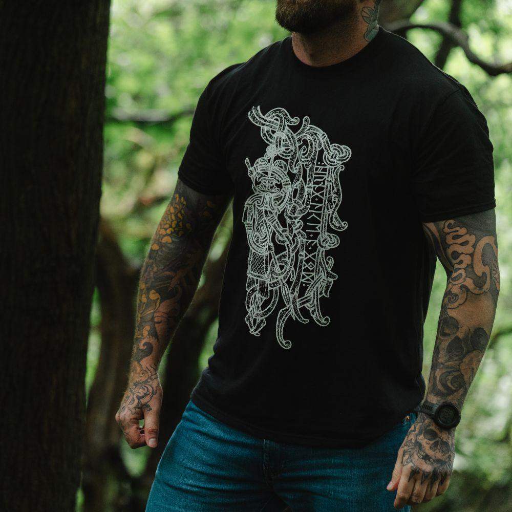 Man in forest wearing black t-shirt with intricate Norse Viking tattoo-inspired design and runes