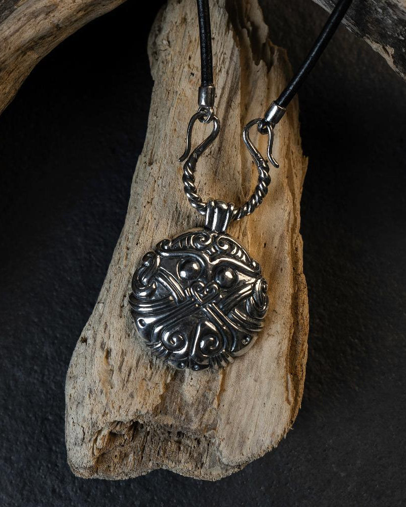 Viking-inspired silver pendant with Norse knotwork, displayed on driftwood, evoking ancient Scandinavian art.