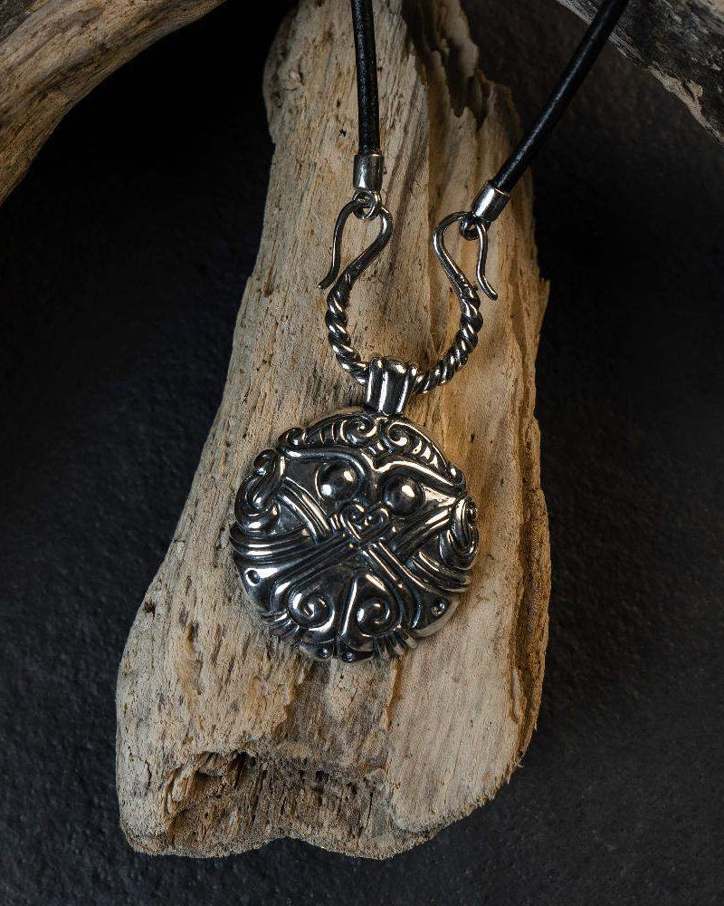 Viking-inspired silver pendant with Norse knotwork, displayed on driftwood, evoking ancient Scandinavian art.
