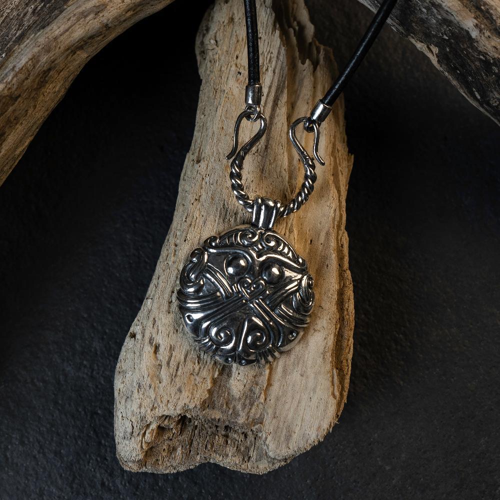 Viking-inspired silver pendant with Norse knotwork, displayed on driftwood, evoking ancient Scandinavian art.