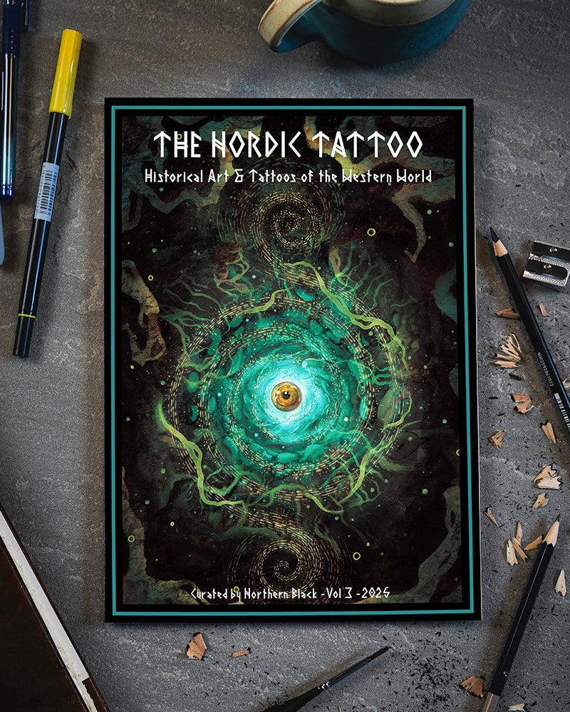 The Nordic Tattoo Vol 3 art book with swirling green eye design, surrounded by pens and pencils on gray desk