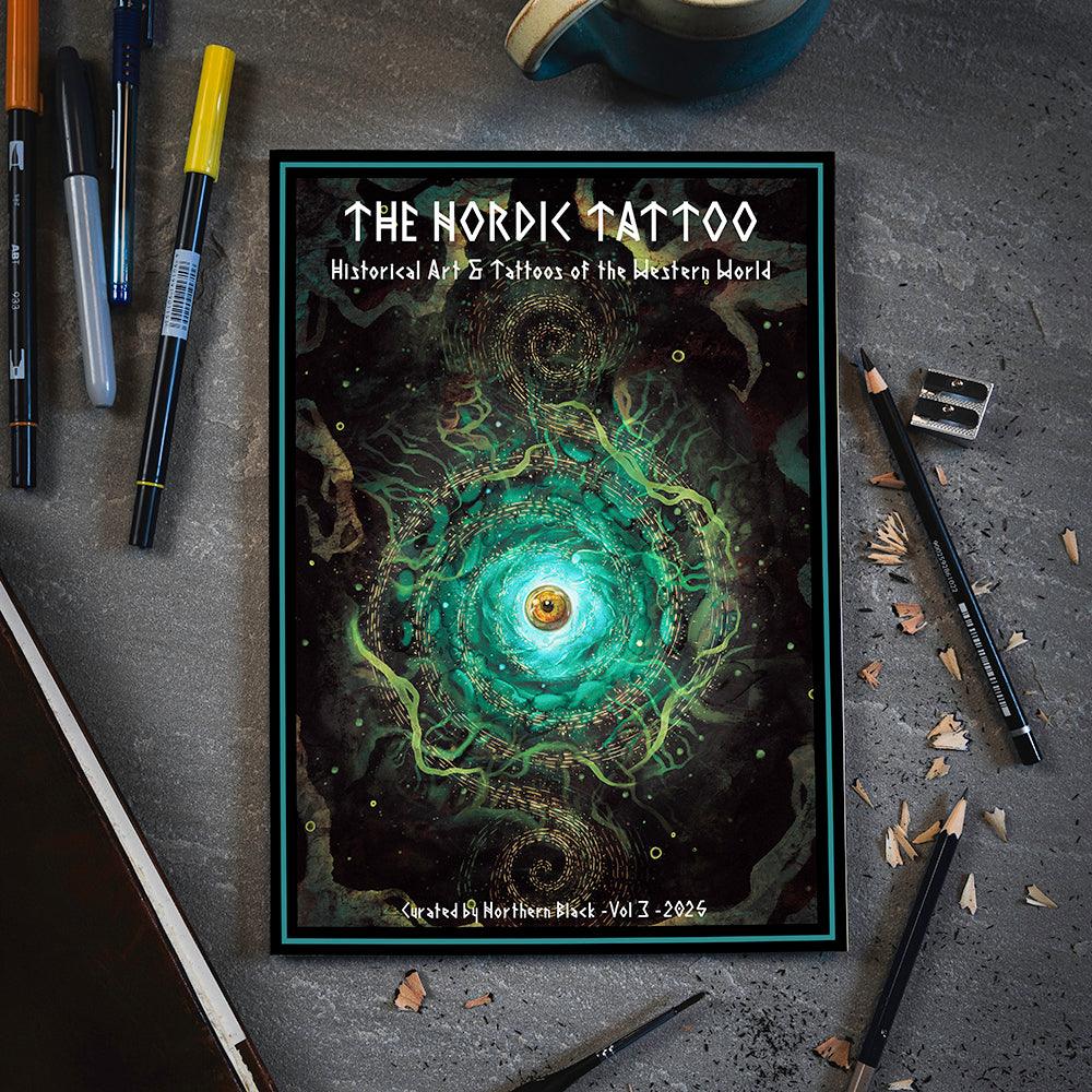 The Nordic Tattoo Vol 3 art book with swirling green eye design, surrounded by pens and pencils on gray desk