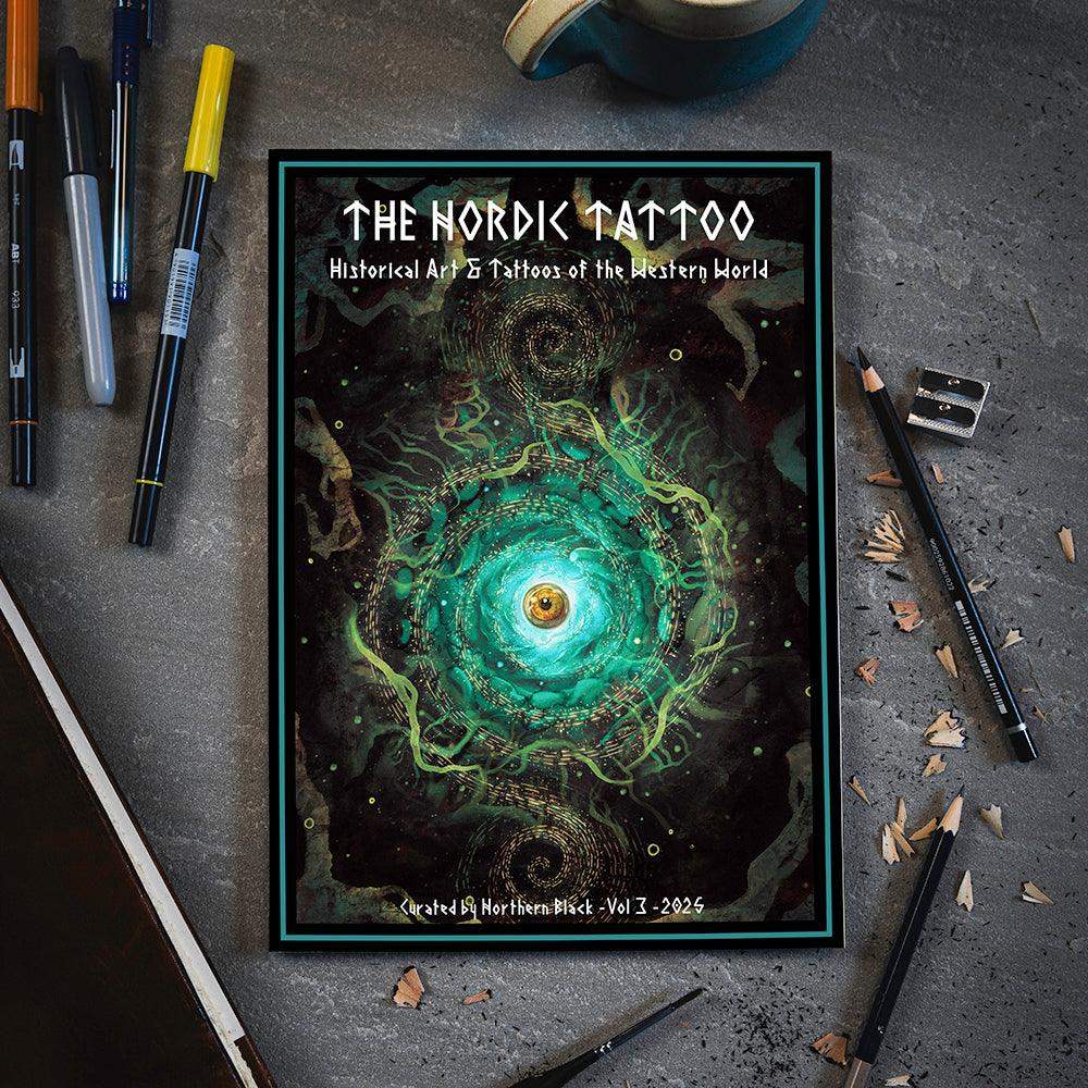 The Nordic Tattoo Vol 3 art book with swirling green eye design, surrounded by pens and pencils on gray desk
