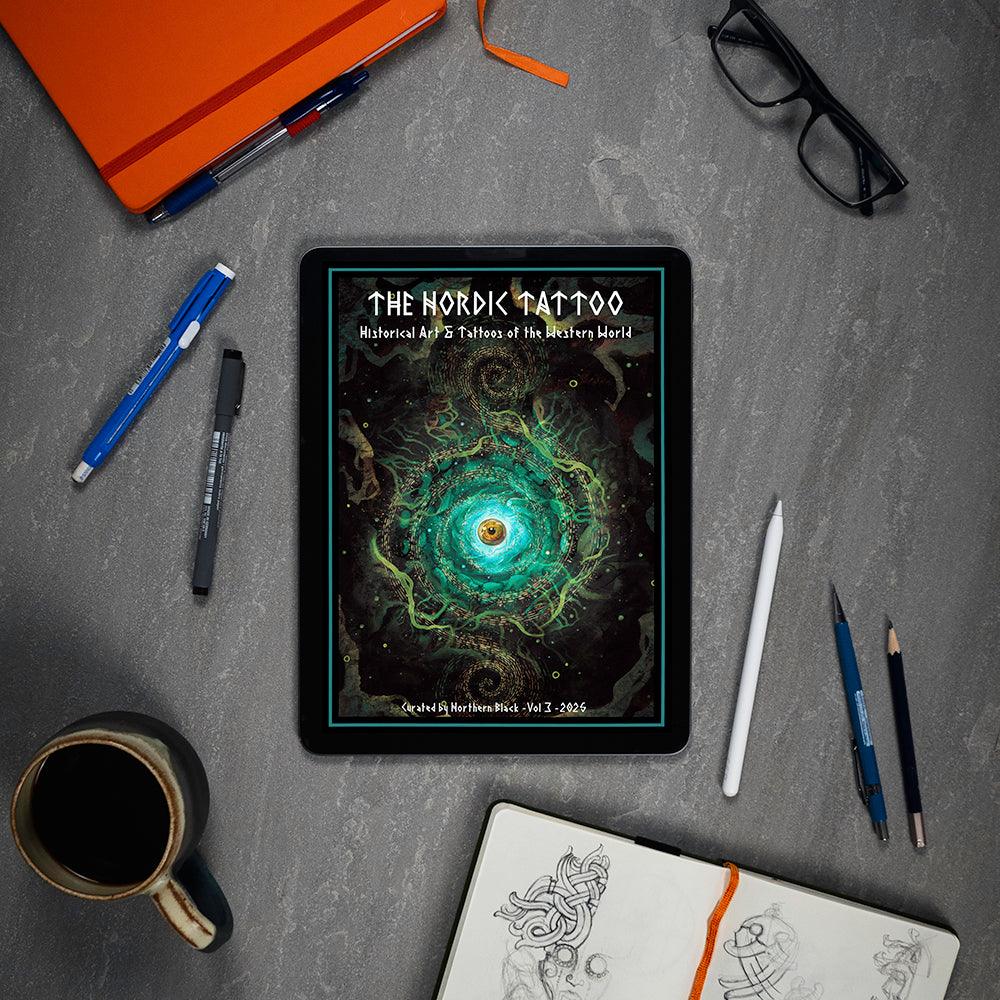 The Nordic Tattoo art book on tablet, surrounded by sketch tools and coffee, showcasing Viking-inspired designs