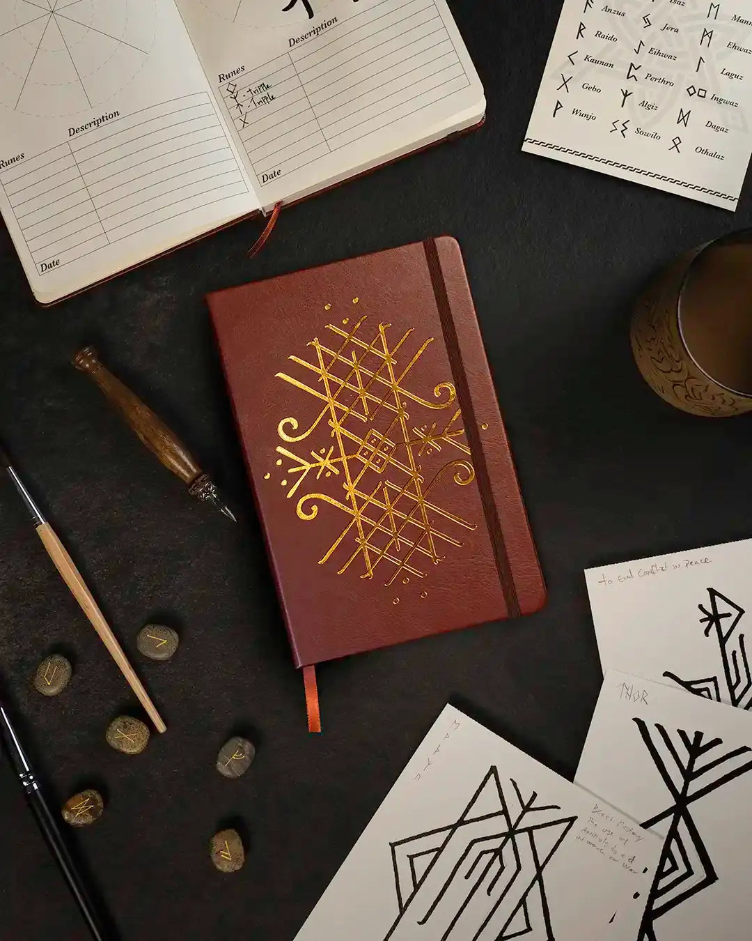 Leather journal with gold Norse rune design, surrounded by rune stones, sketches, and Viking-inspired art tools
