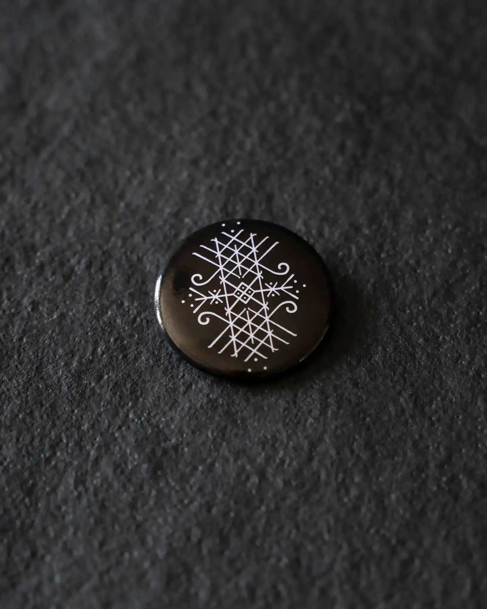 Black enamel pin with white Norse rune design on dark textured background