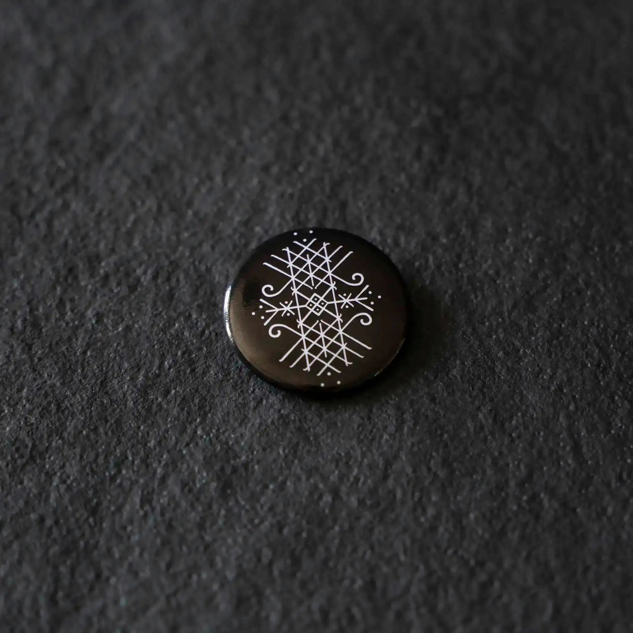 Black enamel pin with white Norse rune design on dark textured background