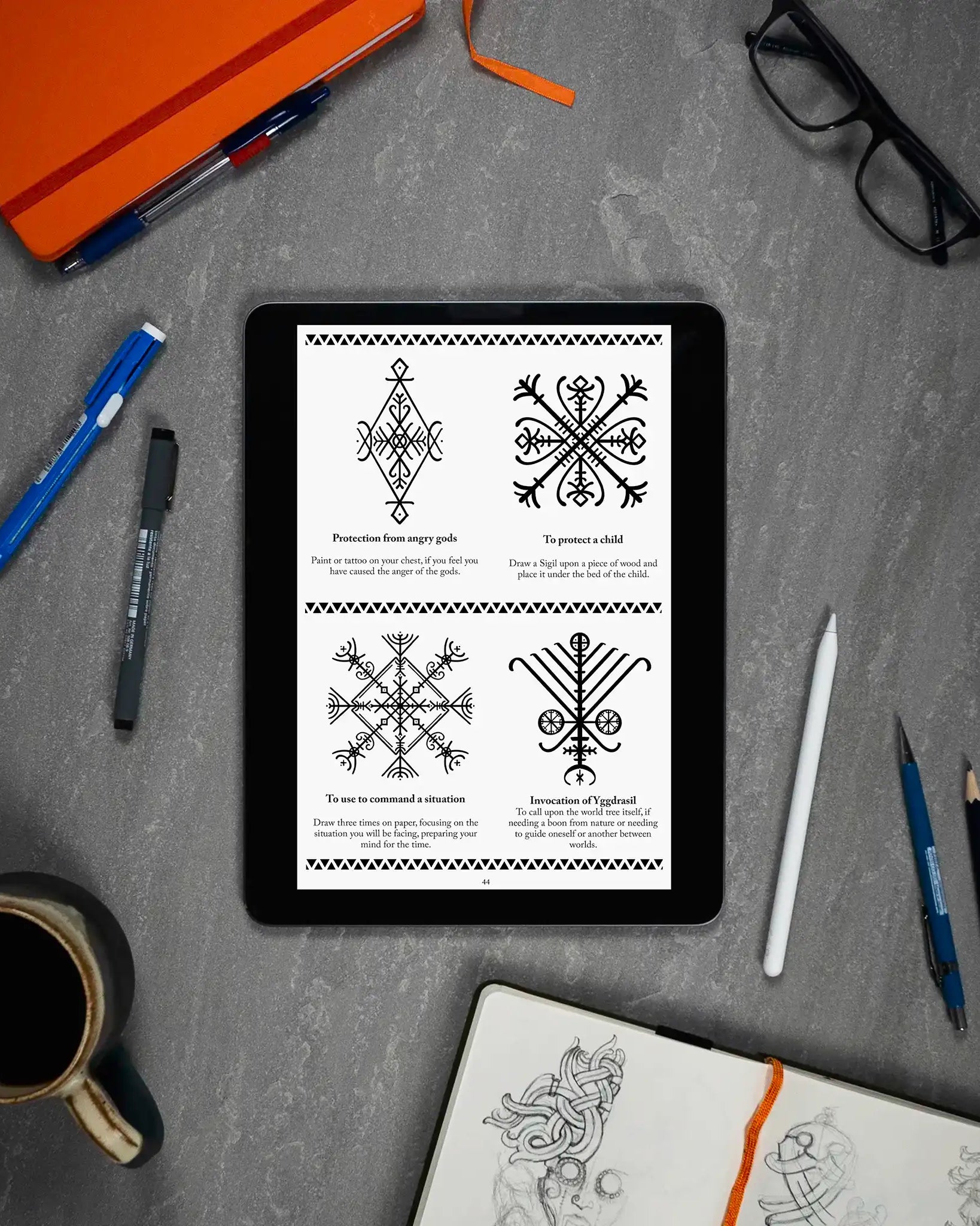 Viking rune designs and Norse symbols displayed on tablet, surrounded by sketchbook, pens, and coffee — ideal for tattoo or ritual use