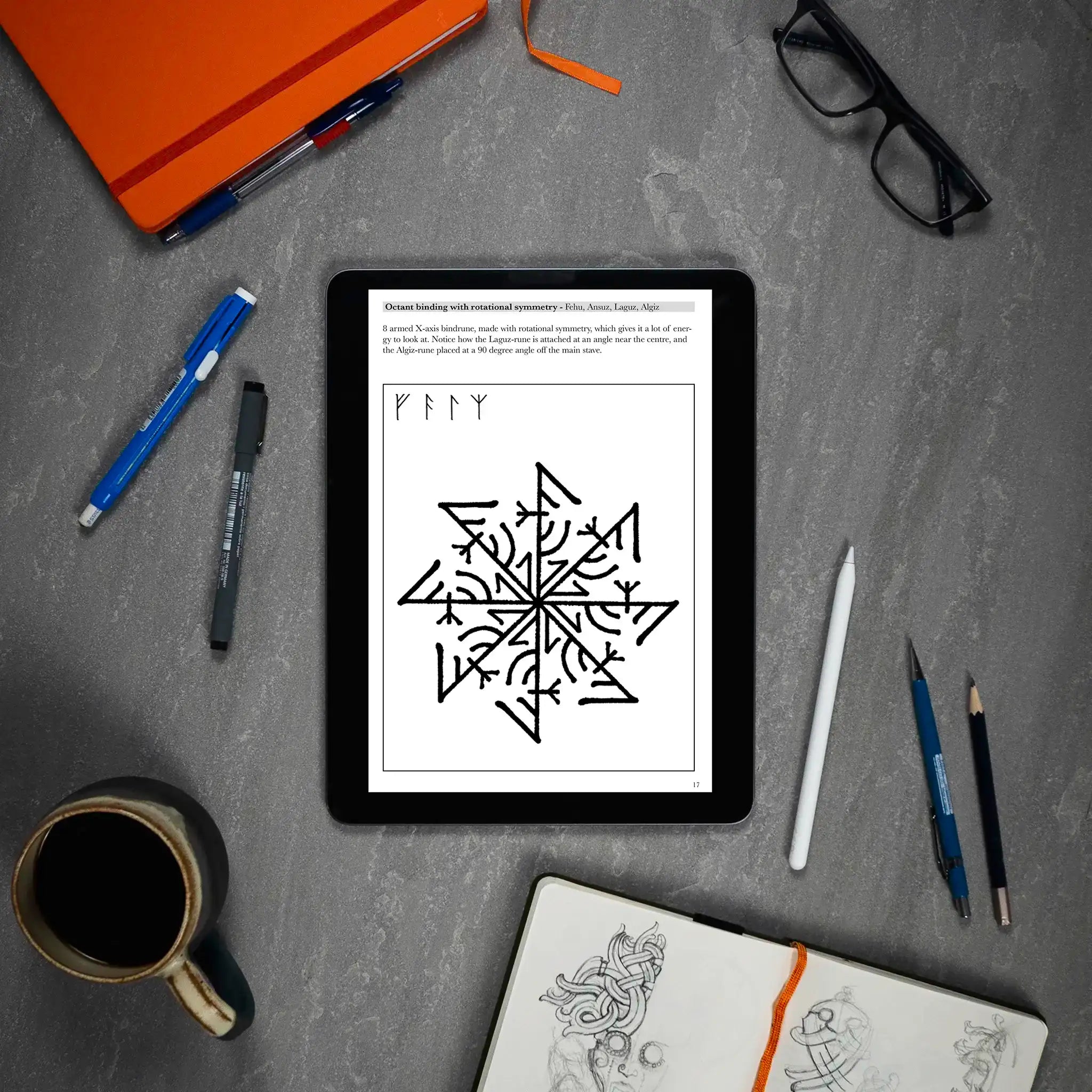 Viking rune design with rotational symmetry displayed on tablet, surrounded by sketchbook, pens, and coffee — Norse tattoo art inspiration