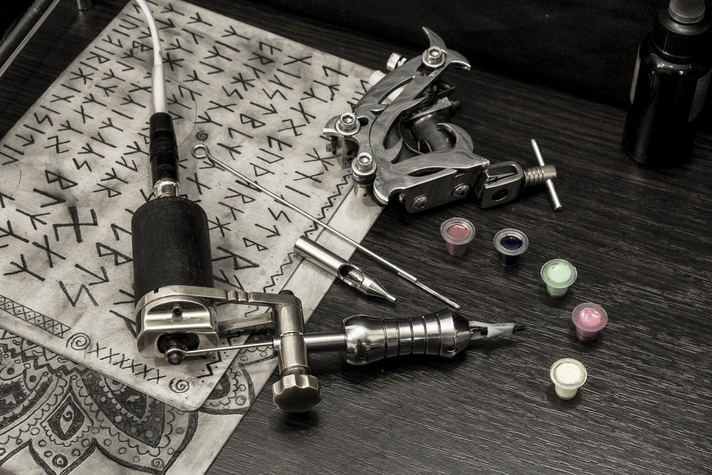 Tattoo machine with needles, ink cups, and Norse runes