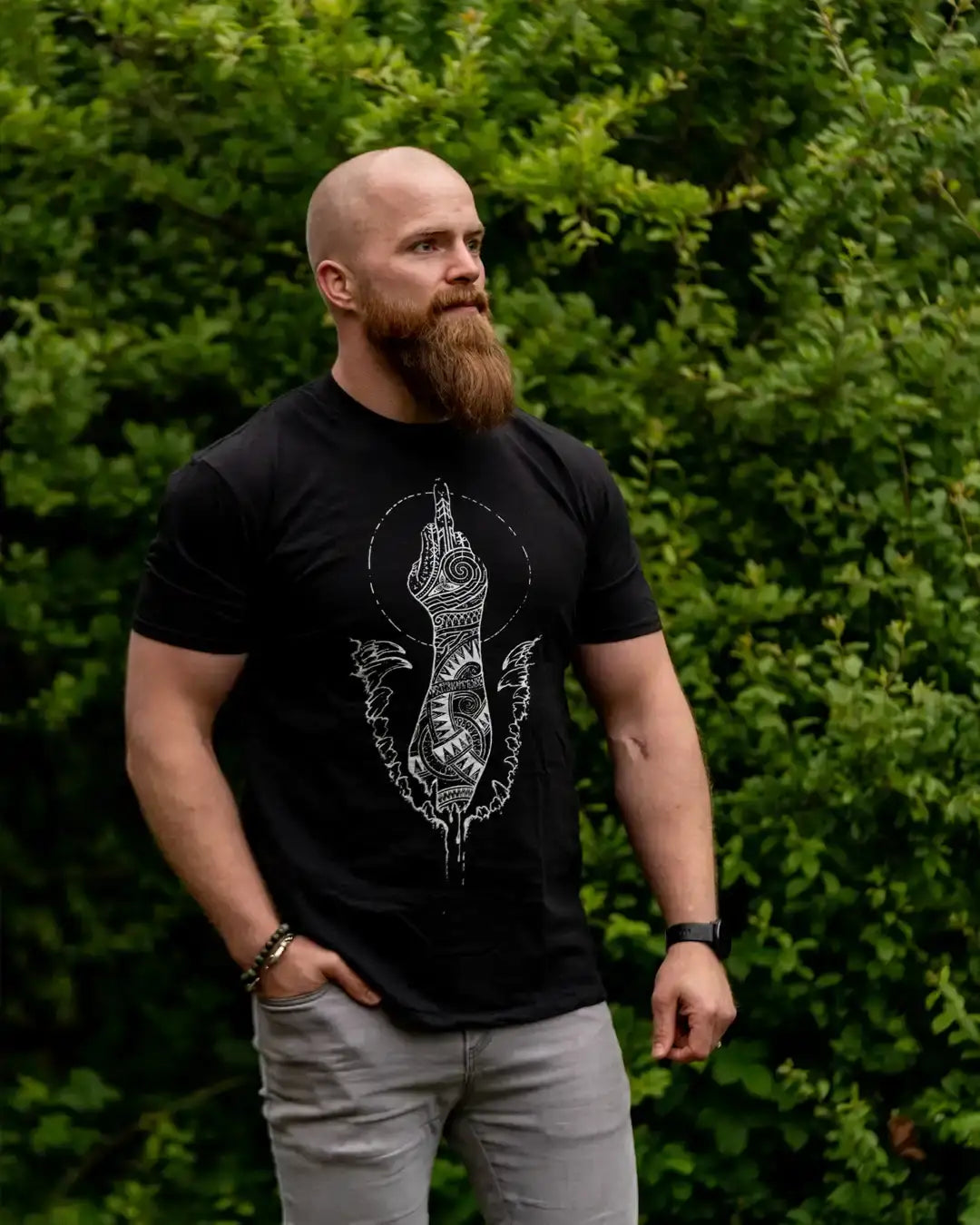 Man wearing black Norse-inspired t-shirt with Viking tattoo art design, standing outdoors