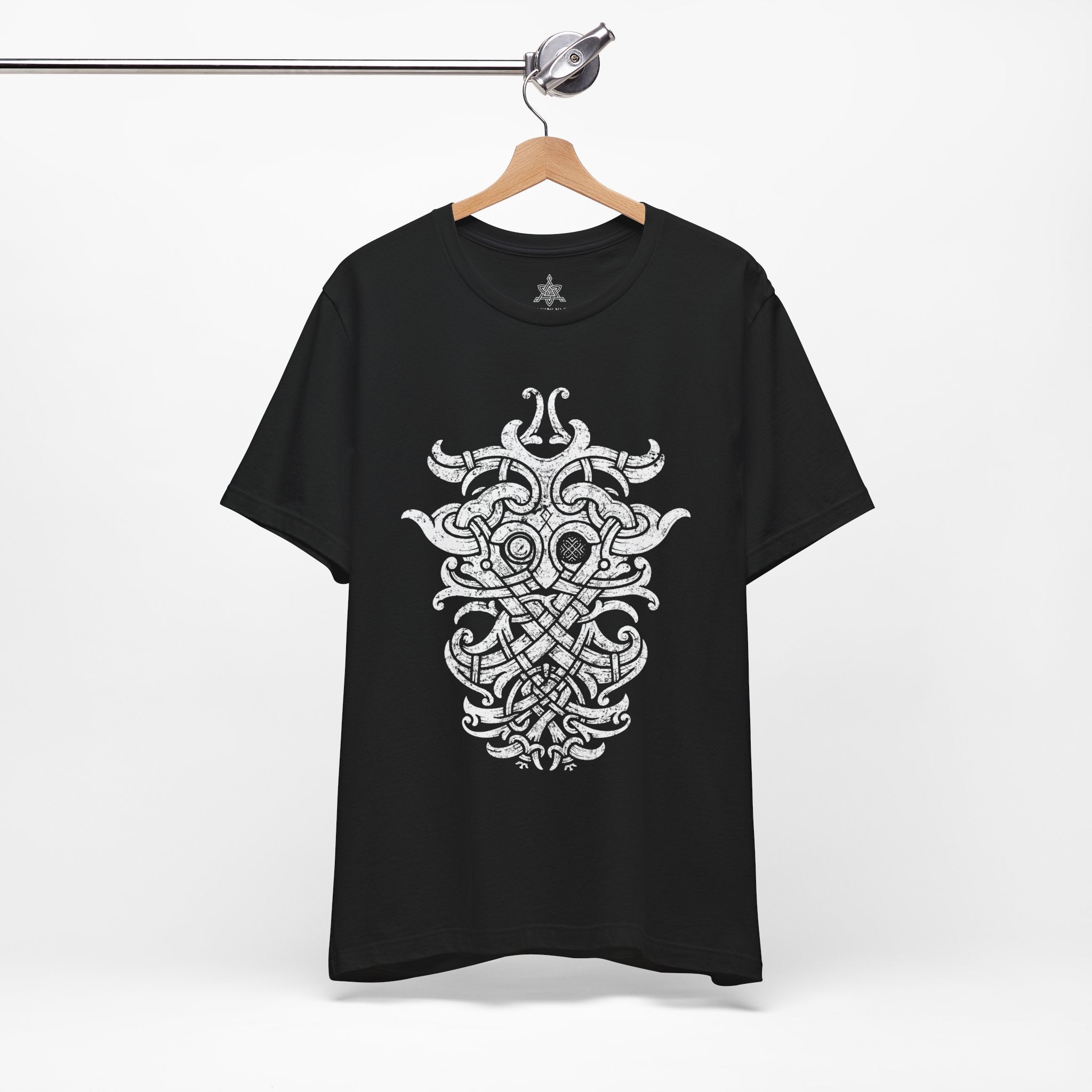 A black short-sleeve t-shirt hanging on a wooden hanger from a metal rack, featuring a large white Norse knotwork design printed on the front.