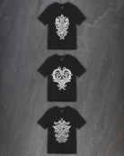 Three black short-sleeve t-shirts with intricate white godmask prints, arranged vertically on a dark gray textured stone background.