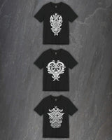 Three black short-sleeve t-shirts with intricate white godmask prints, arranged vertically on a dark gray textured stone background.