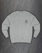 Front of a heather grey Lifthrasir sweatshirt with a small Northern Black logo on the chest on a dark slate background