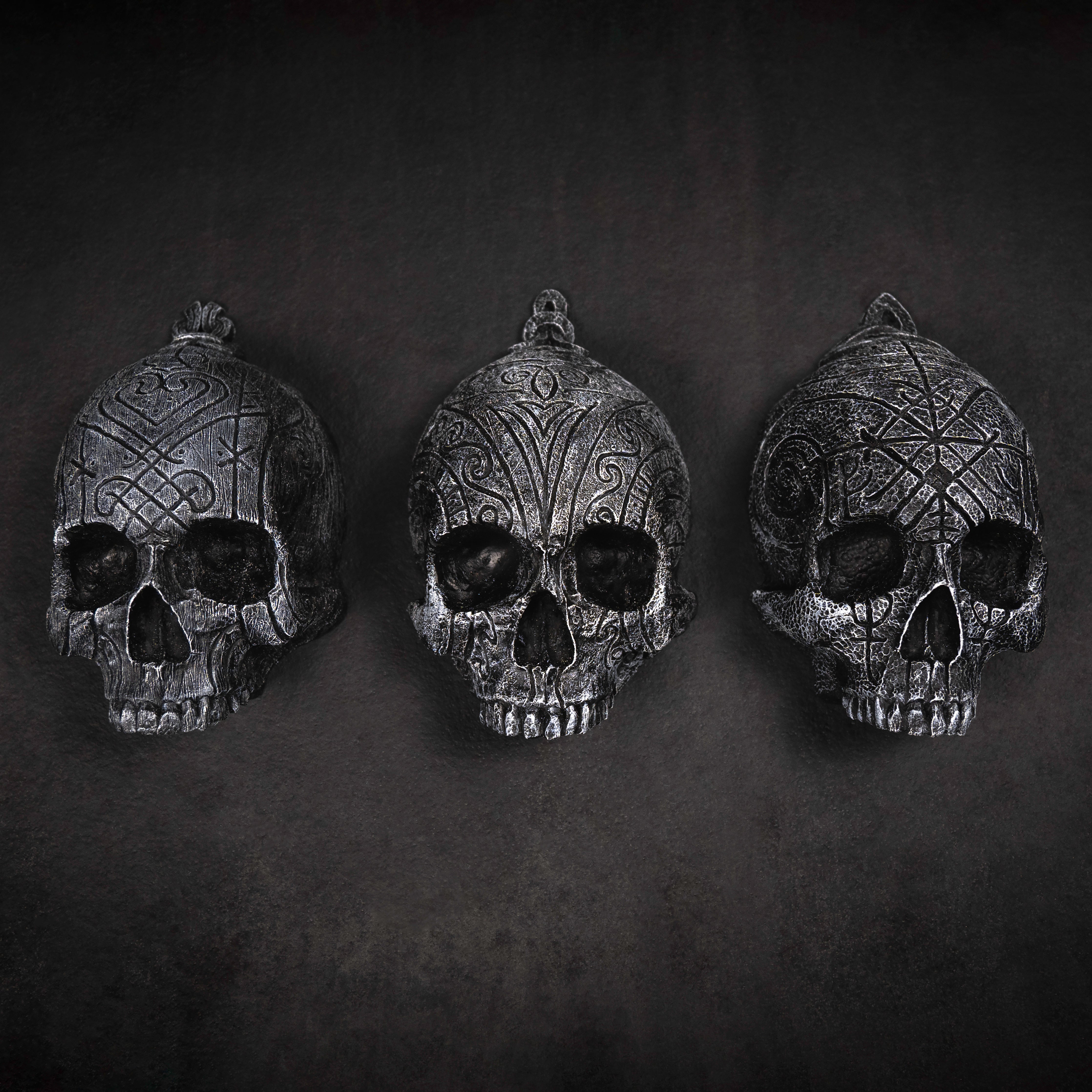 Depicting three skulls that are in a collection. They are resin human shaped skulls with runes on them, each representing one of the following: Love, Lust, Loss.