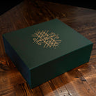 Dark green gift box with gold Norse knotwork design, resting on rustic wooden surface